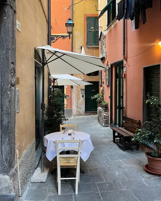 A table set in a narrow Ligurian lane, with green shutters and laundry overhead